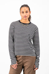A woman modeling a black and white horizontally striped long-sleeve knit top with a crew neck, paired with brown pants, against a plain white studio background.
